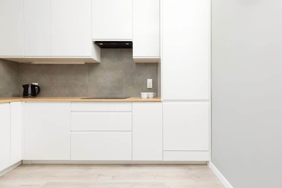 A bright kitchen featuring a large window, white cabinetry, and a modern sink setup.