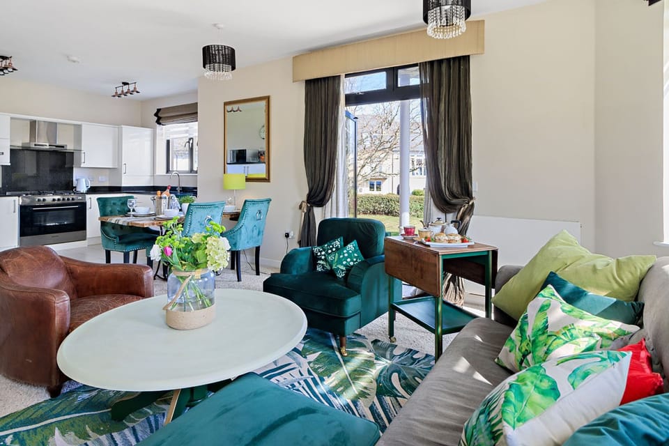 Living area with kitchen, double sofa, two arm chairs, TV, and dining table