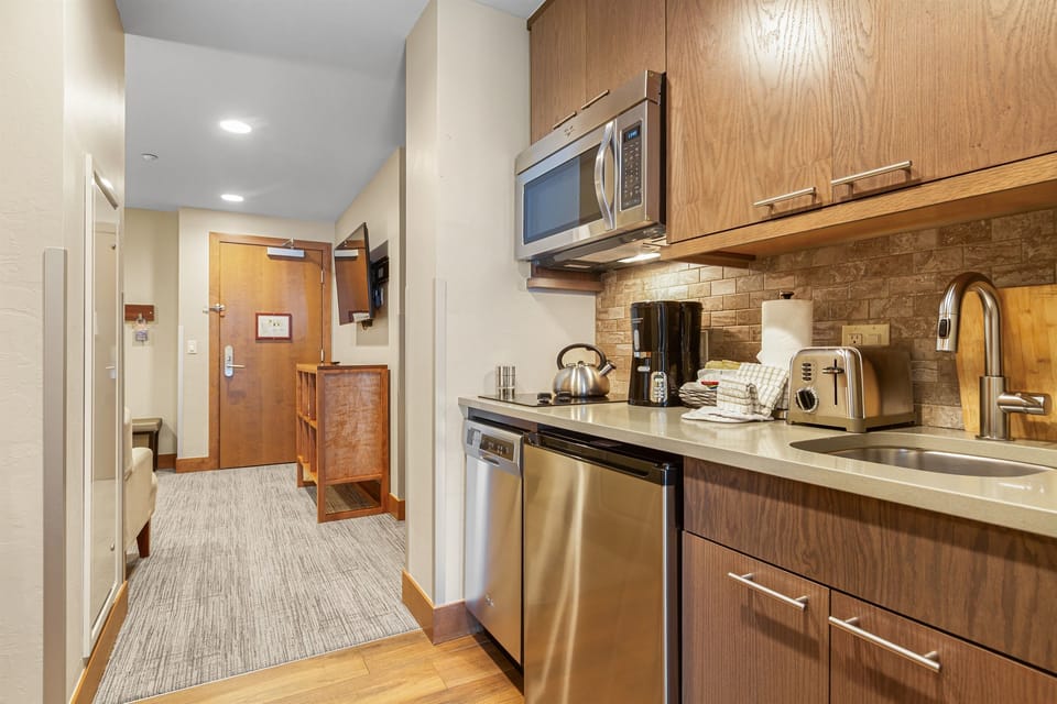 Well-equipped kitchenette featuring stainless steel appliances, a microwave, sink, coffee maker, toaster, and ample cabinet space for preparing meals and snacks during your stay.
