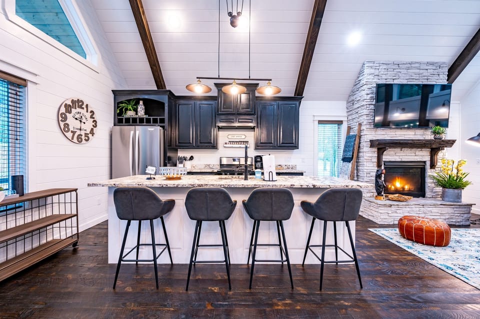 Fully stocked kitchen with ice machine, a dining table for six, and an open living room with a fireplace and TV above the mantle provide comfort and style.