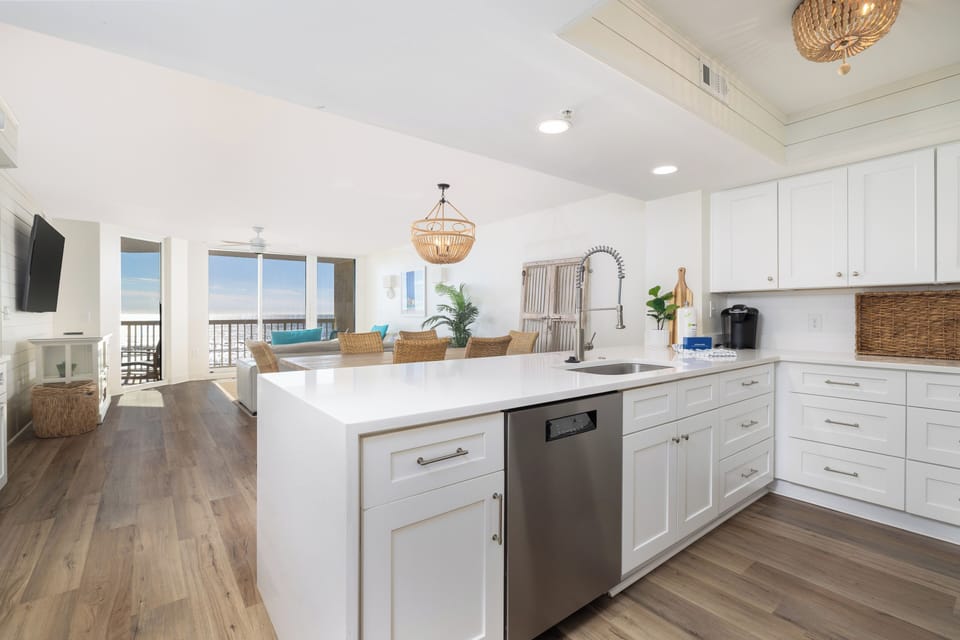 Your dream beach kitchen awaits with pristine white cabinetry, quartz countertops, and stunning ocean views through expansive windows.