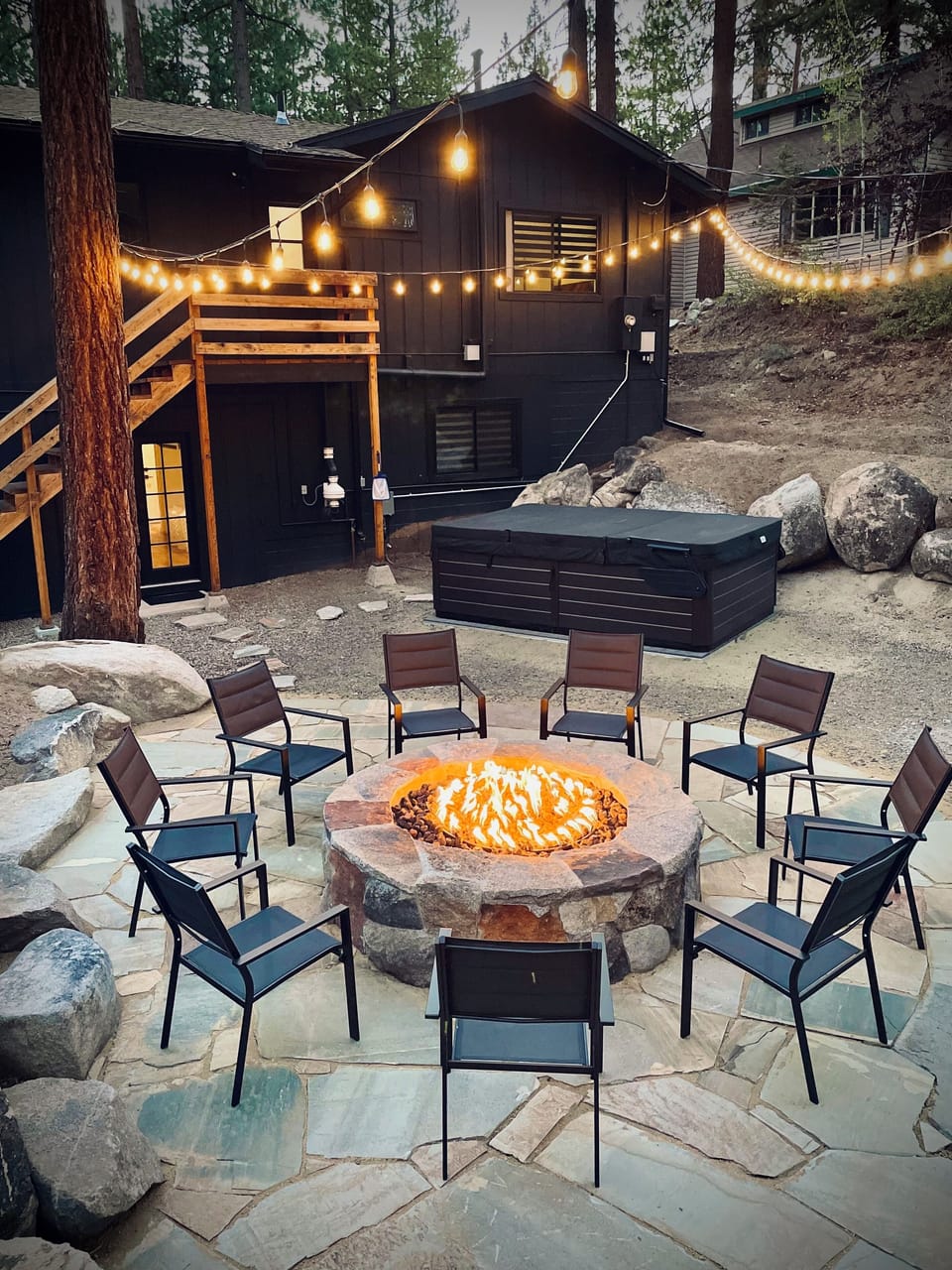 Backyard with fire-pit, hot tub, and string lights on the edge of the forest