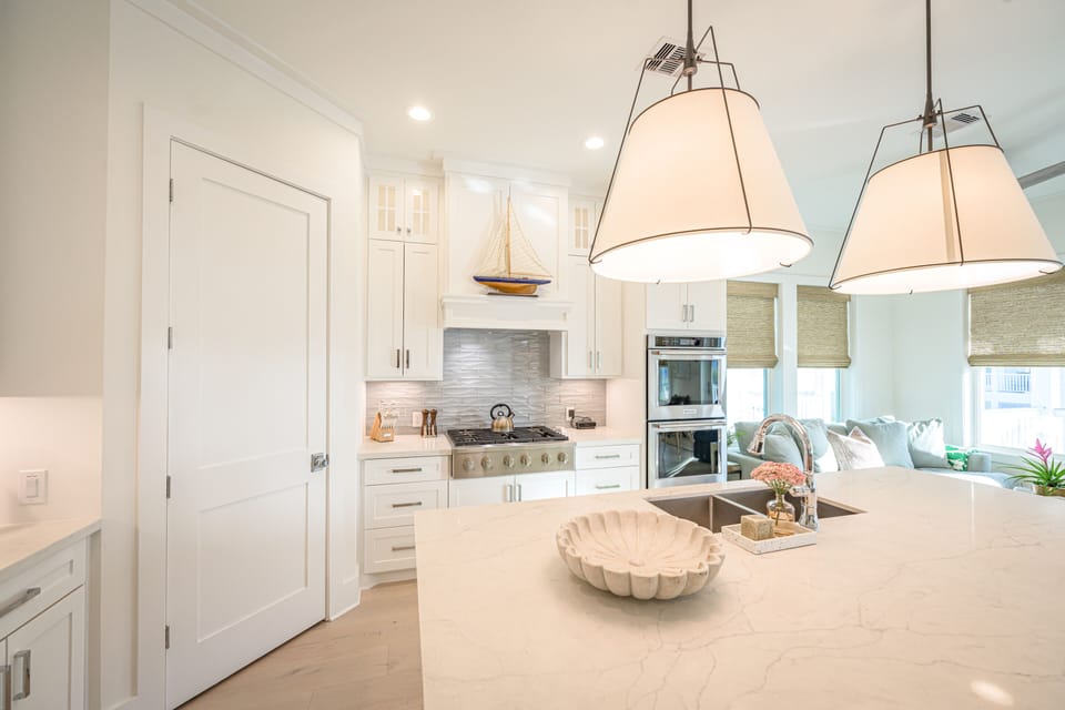 View of pantry door, island, sink, stove top and double oven. 