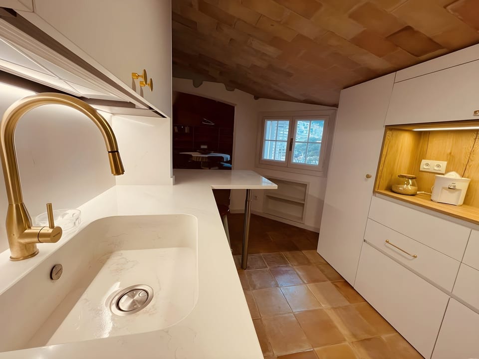 This photo captures a detail of the modern and functional kitchen, featuring a sleek gold faucet over a white marble sink. The countertop is spacious and ideal for preparing meals. The kitchen is thoughtfully equipped with everything you need for a comfor