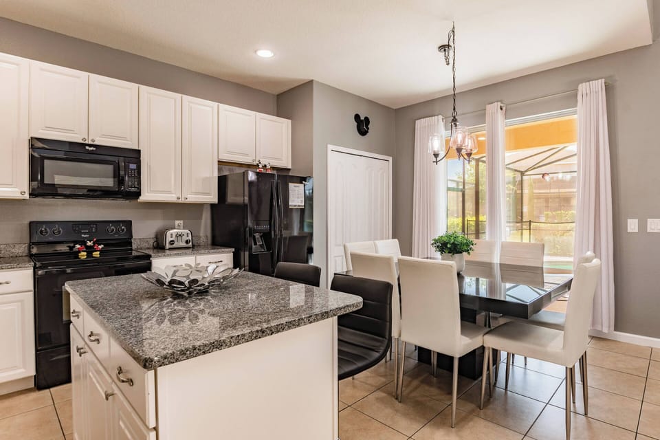Experience this modern kitchen with its sleek white cabinetry and dark granite island. Natural light floods the roomy dining area, featuring chic chairs that invite you to gather and enjoy memorable moments with loved ones.