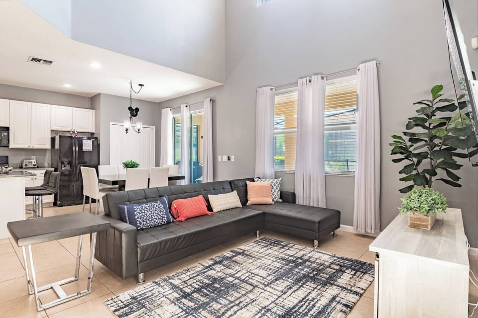 Enjoy the inviting spacious living area with a sleek dark sofa and colorful throw pillows, perfect for relaxation. Large windows let in natural light, while a stylish area rug adds warmth to the modern decor.