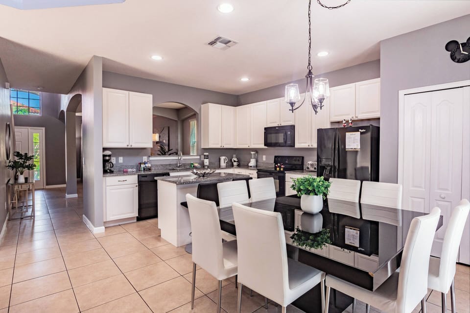 Welcome to a stylish kitchen with sleek white cabinets and glossy black countertops. The spacious dining area, illuminated by modern pendant lighting, is ideal for cozy gatherings and enjoyable meals with friends.
