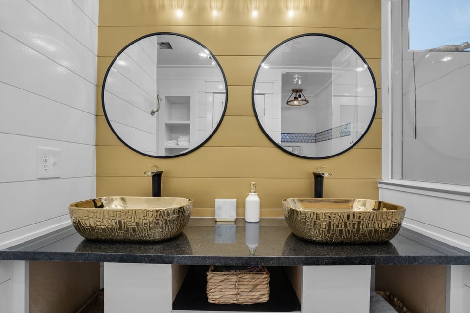 Pamper yourself in this stunning dual-sink bathroom with artistic vessel bowls, elegant gold accents, and thoughtful amenities for your daily routine.
