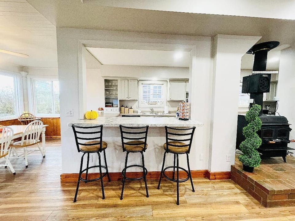 Cozy breakfast bar with seating for three, overlooking a well-equipped kitchen. Nearby, a wood-burning stove adds charm and warmth. Adjacent sunroom and dining area create a perfect flow for meals and gatherings during your vacation stay.






