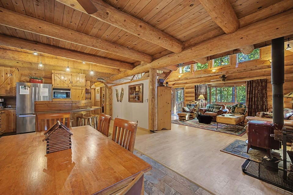 Gather around the rustic dining table in this stunning log cabin, where exposed beams and cozy wood-burning stove create the perfect mountain retreat atmosphere.