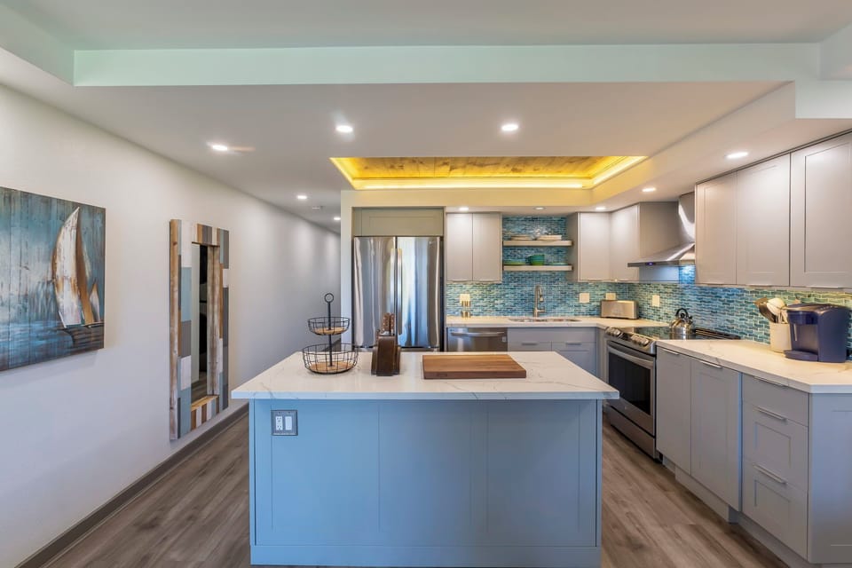 A bright, fully-equipped kitchen awaits your culinary adventures, featuring sleek cabinetry, a spacious island with seating, and stylish coastal-inspired tile accents that evoke seaside charm.