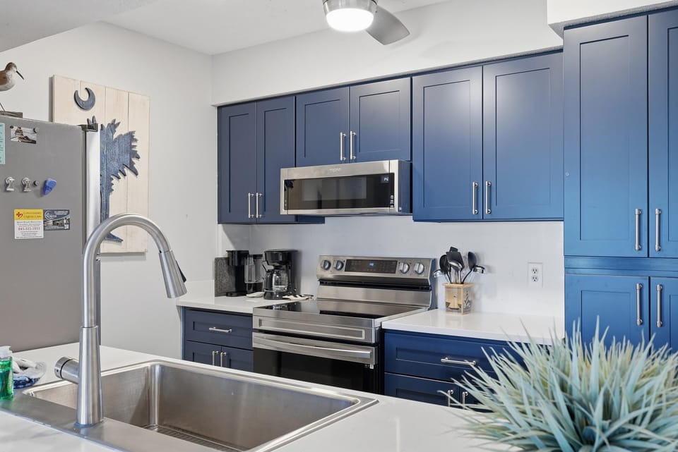 Stainless steel sink and appliances contrast with deep blue cabinetry in the bright kitchen.