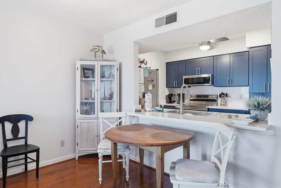 Dining nook with a wooden table, mix of black and white chairs, and a white display cabinet beside the kitchen window.