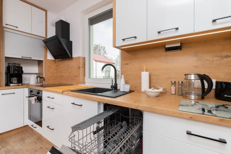 A modern kitchen with built-in appliances, including an oven, stovetop, and dishwasher, alongside wooden cabinets and a window.