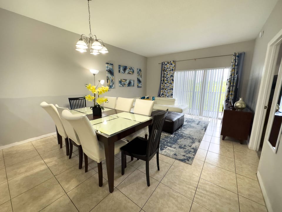 Enjoy meals at the stylish glass table surrounded by plush white chairs in this bright dining area, where natural light pours in through expansive sliding doors, creating a fresh and cheerful atmosphere perfect for relaxation.