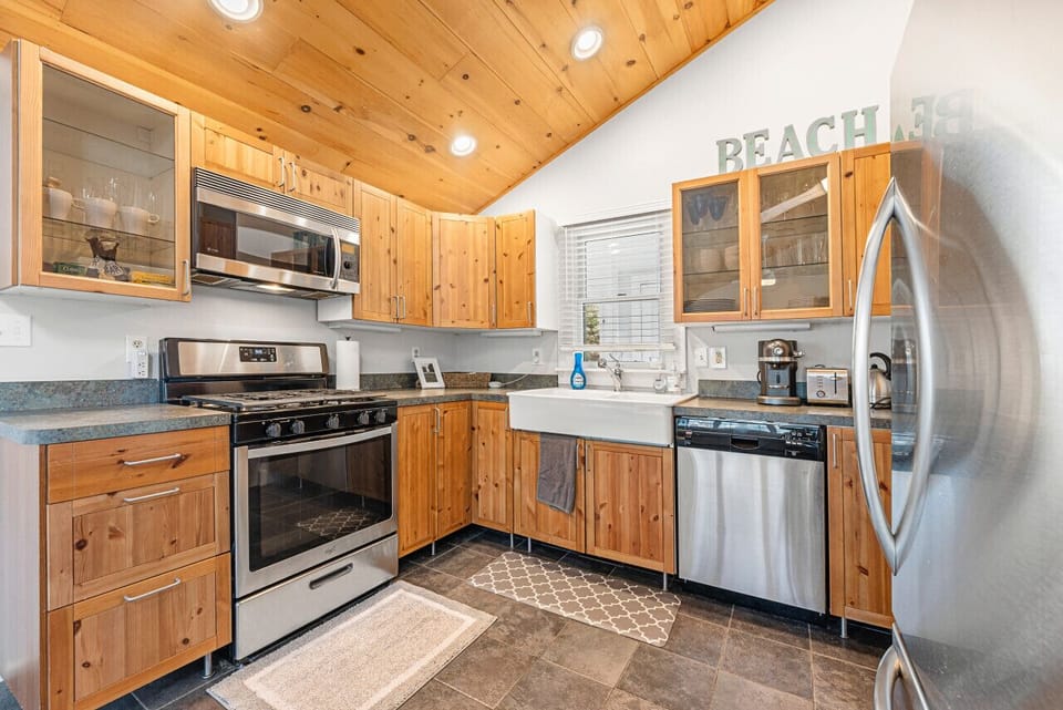 Inviting kitchen with rustic wood ceiling, ample space, and sleek wood cabinets complemented by stainless steel appliances.