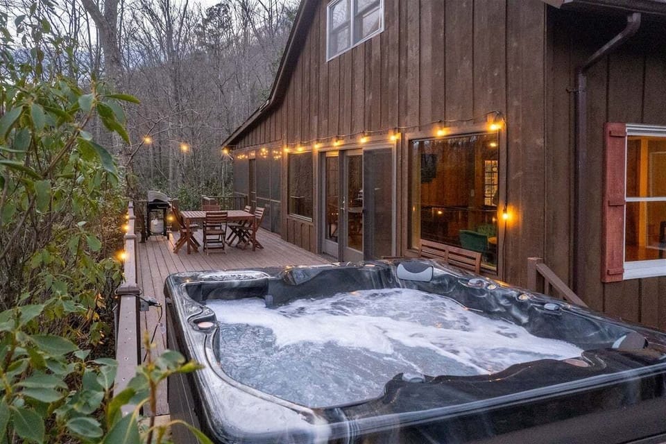 Steaming private hot tub on the outdoor deck illuminated by warm string lights at dusk.