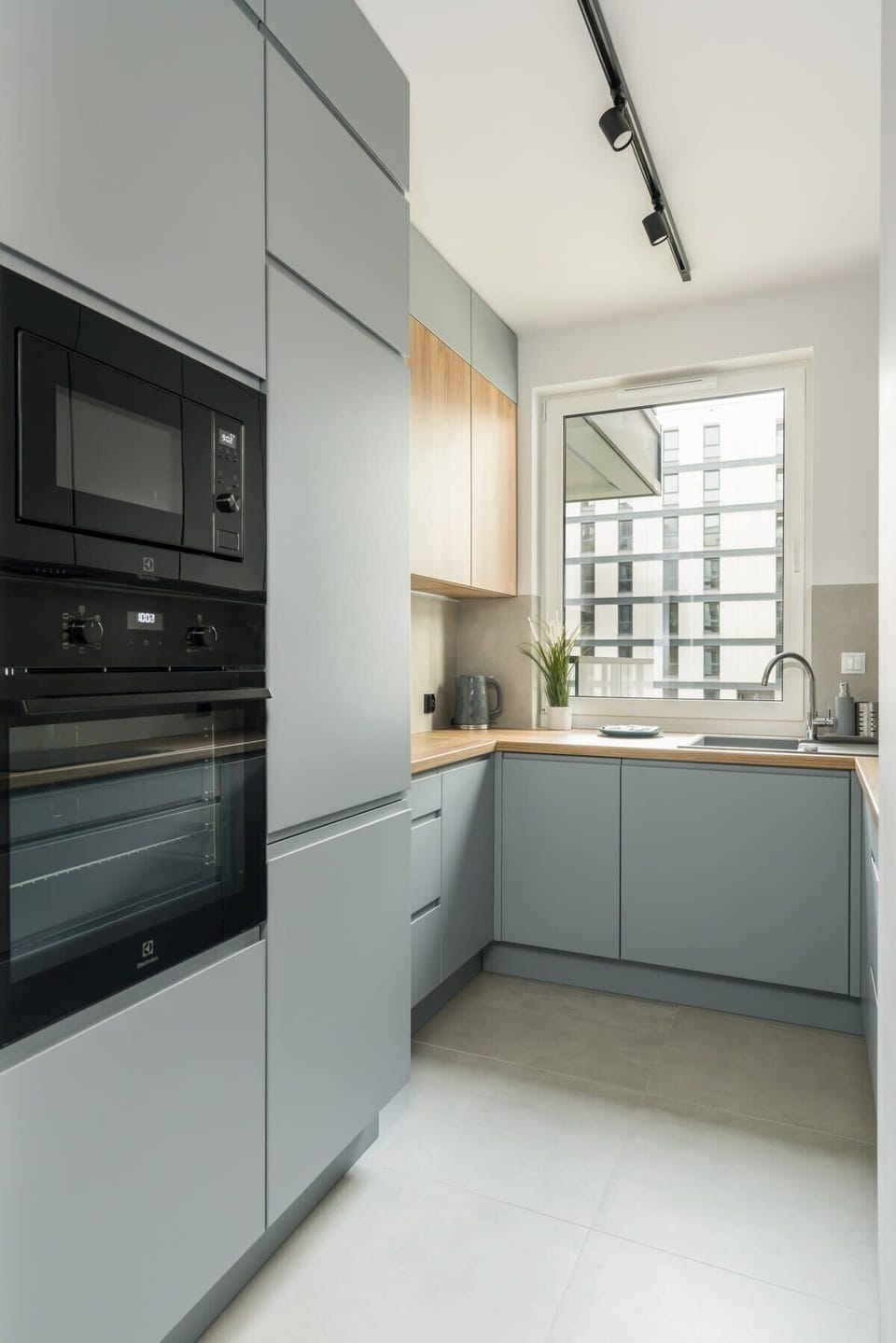 Modern kitchen area with a light gray color palette and natural light streaming in from the windows. Oven and microwave.
