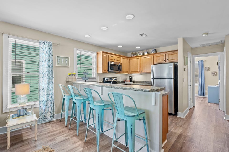 Your open-concept kitchen welcomes you with granite counters and bright turquoise bar stools, perfect for morning coffee or casual meals together.