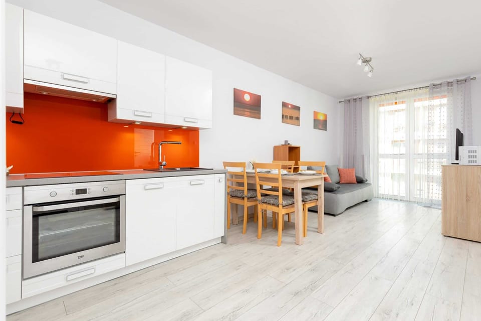 A kitchen with white cabinets and an orange backsplash. The space is clean, modern, and includes built-in appliances.

