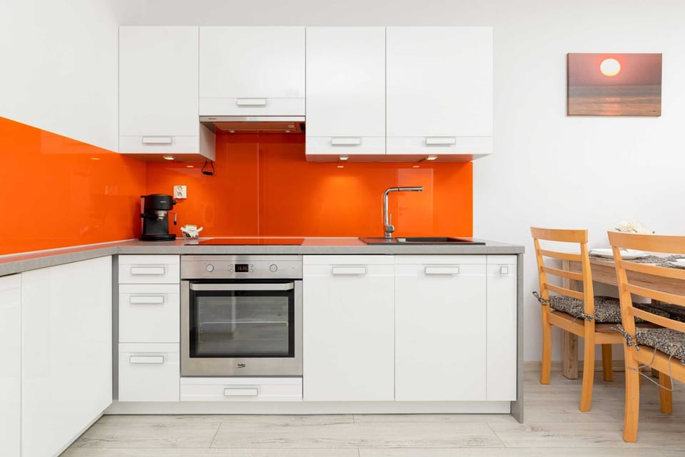 Another angle of the kitchen with cabinets, countertops, and an oven. The bright orange backsplash stands out.