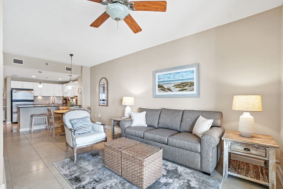 Relax in your bright open living space with coastal artwork and plush seating that flows seamlessly into the modern kitchen.