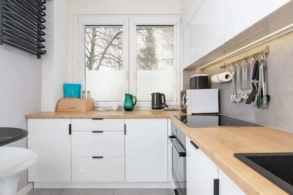 A bright and spacious kitchen with white cabinets, wooden countertops, and modern appliances. A window lets in natural light.