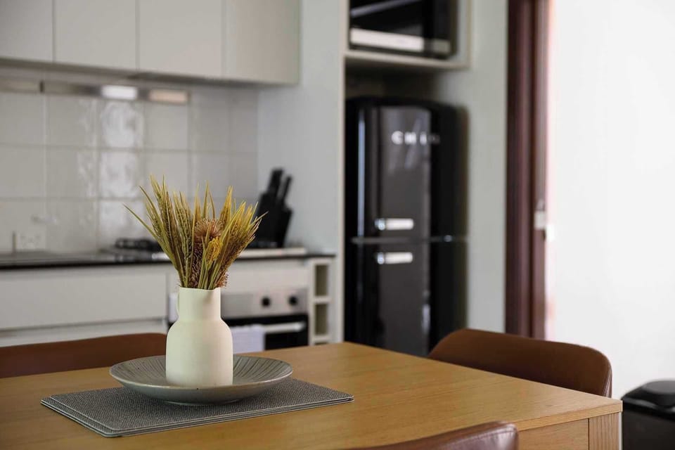 Prepare meals with ease in our beautifully appointed kitchen, featuring a retro-style refrigerator, oven, stove, and all essential utensils. Enjoy dining at the charming table, complete with a fresh floral accent. Your culinary comfort awaits.