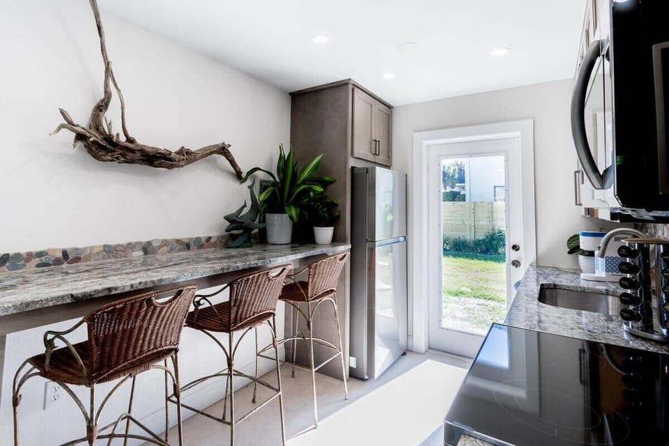 Modern kitchen with natural light and a breakfast bar featuring wicker stools.