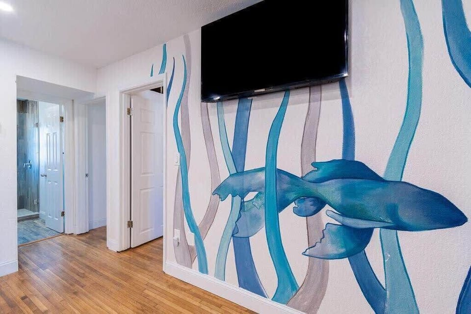 Wall mural with blue aquatic design beneath a mounted flat-screen television in a bright hallway.