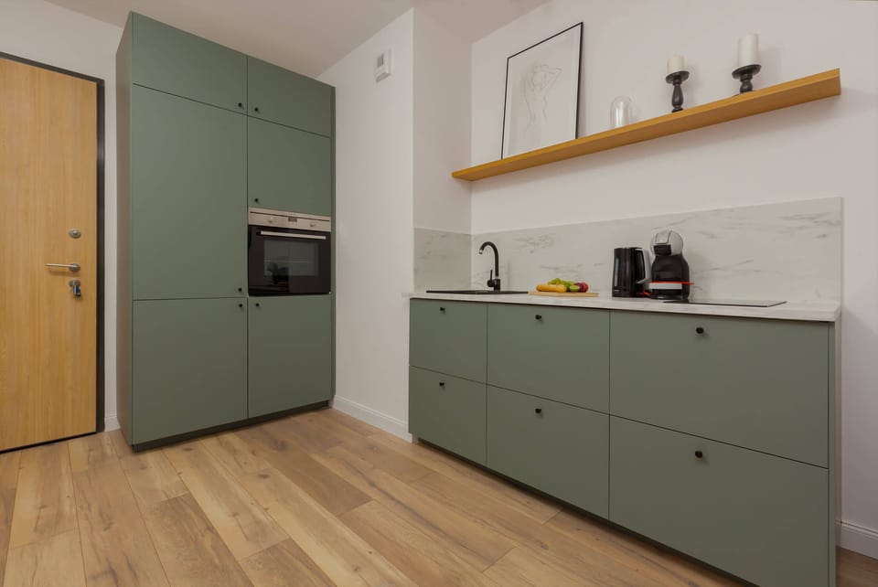 Another view of the kitchen showing continuity in design with green cabinetry, wooden shelves, and decorative elements like plants.