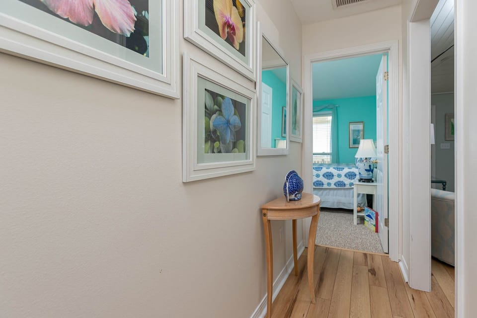 This hallway features vibrant floral artwork and leads to a cheerful bedroom with aqua walls and cozy decor
