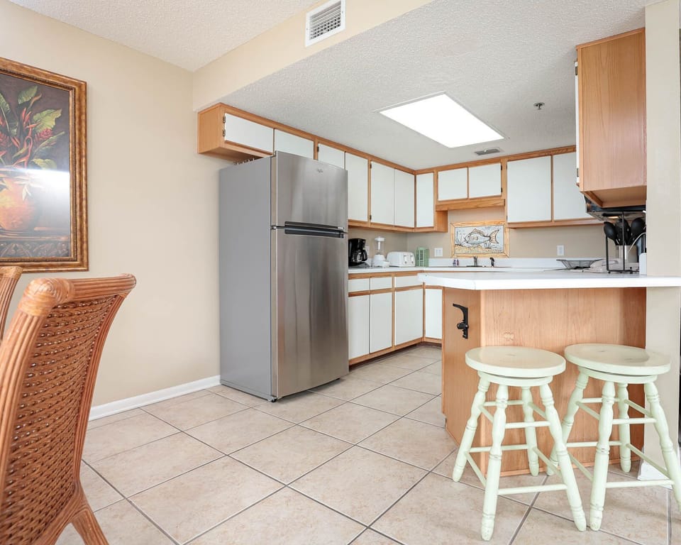 Kitchen area featuring a stainless refrigerator, white cabinetry, and a breakfast bar with mint green stools
