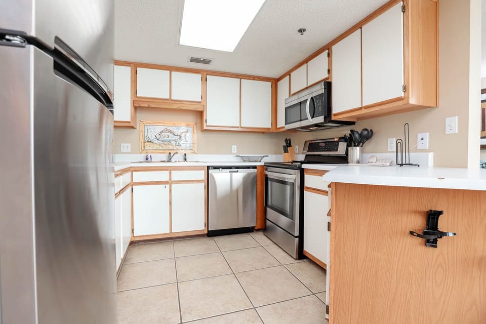 Bright kitchen features light cabinetry, stainless appliances, and a decorative fish mural, creating a cheerful cooking space