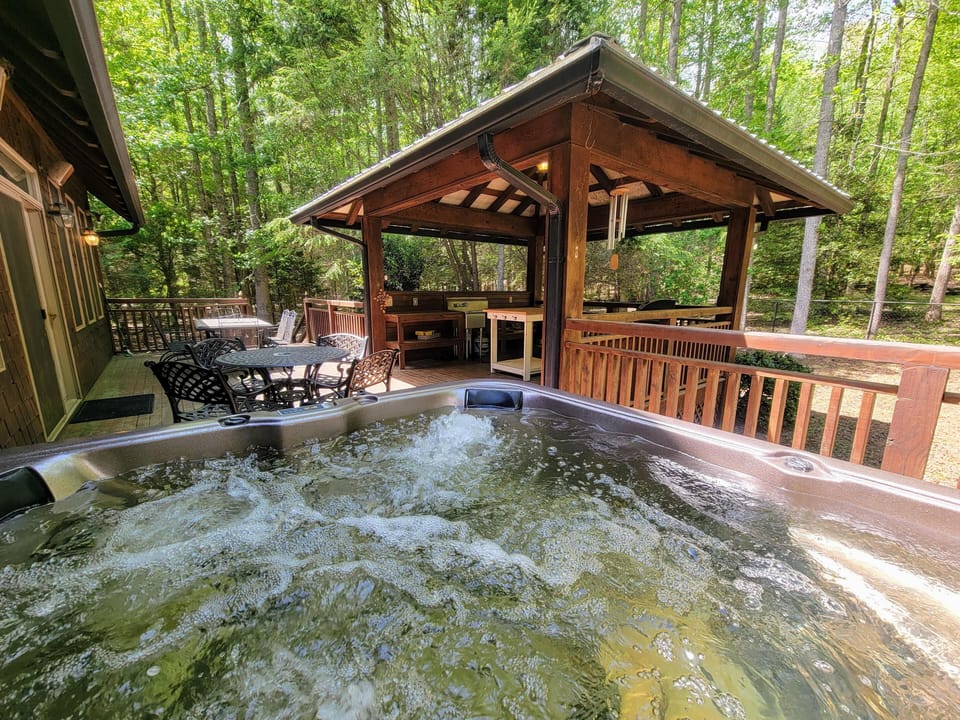 Large deck surrounded by trees includes two seating areas, outdoor kitchen, and 5 person hot tub