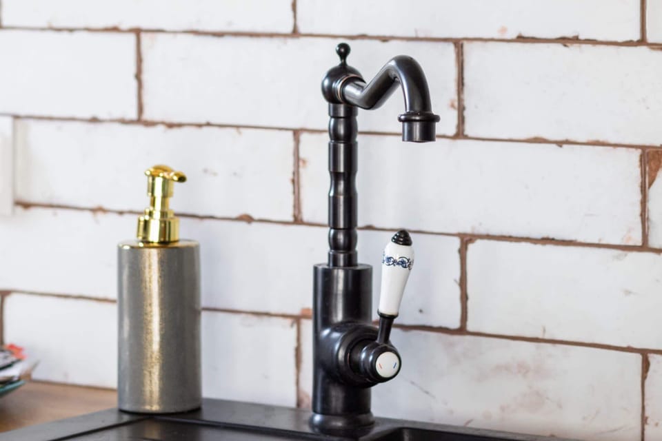 A close-up of a black kitchen faucet mounted against white brick-patterned tiles, adding a rustic touch.