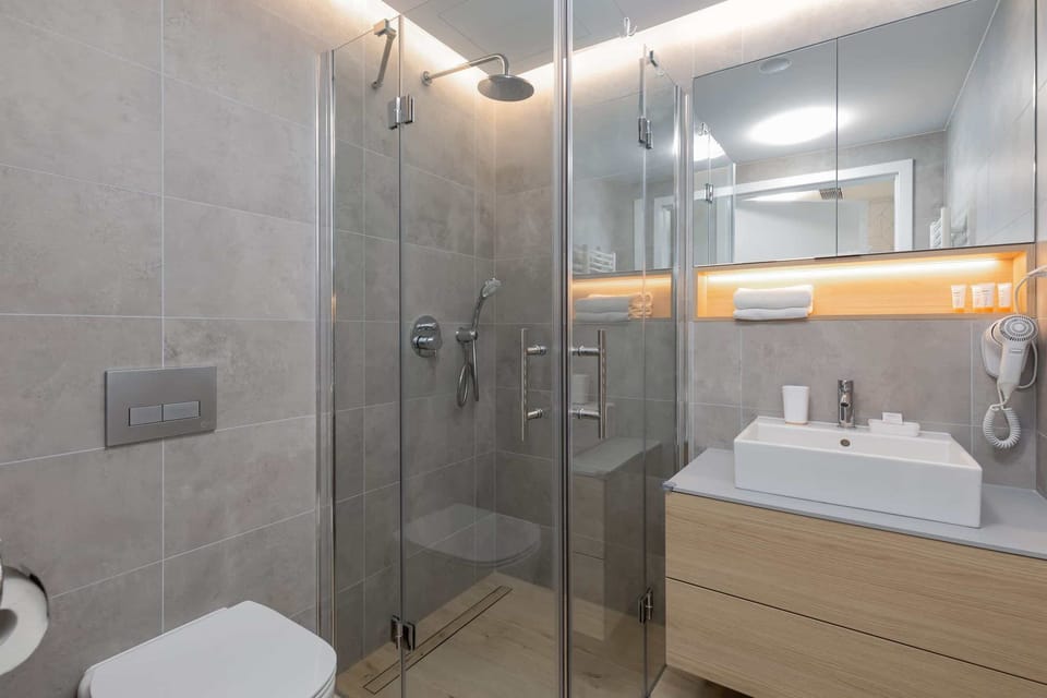 A minimalist bathroom design showcasing a vanity with a lighted mirror and wooden cabinetry.