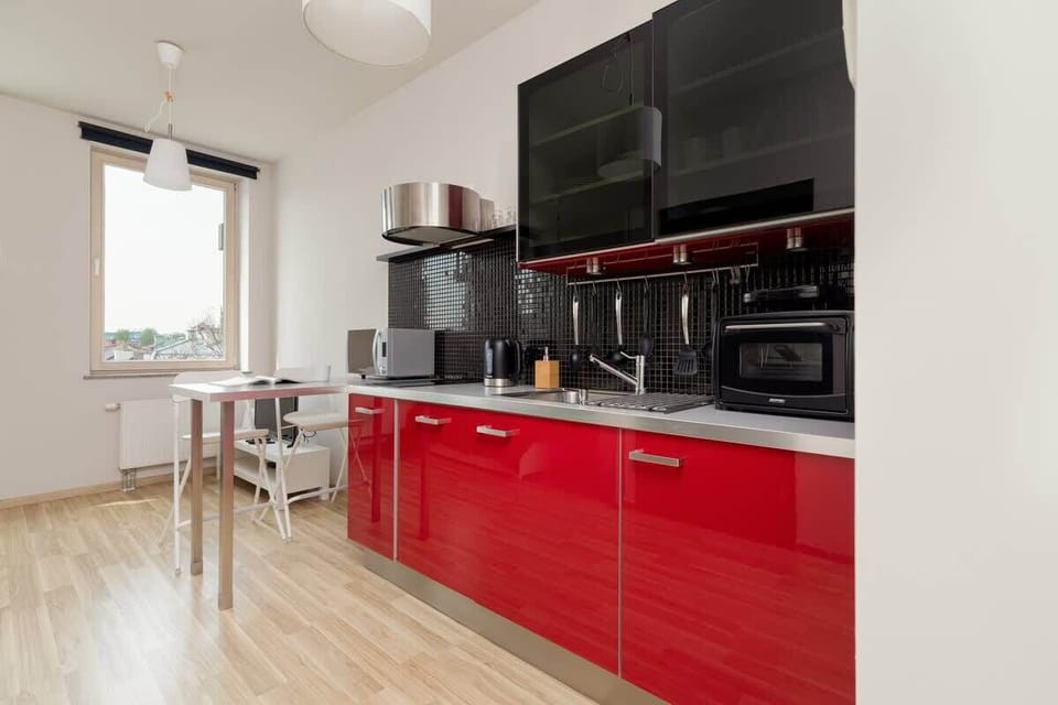 A combined kitchen and living area with red cabinets, a large flat-screen TV, and a spacious layout.
