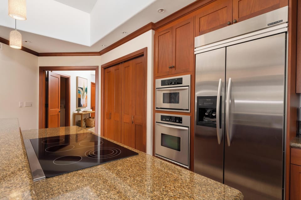 You'll love preparing meals with premium stainless-steel appliances, sleek induction cooktop, double ovens, and abundant cabinet space—all wrapped in warm wood tones and polished granite counters for your comfort.