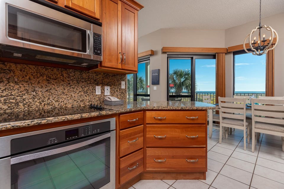 Rich cabinetry complements the granite countertops in this kitchen area, featuring a dining table with a gulf view