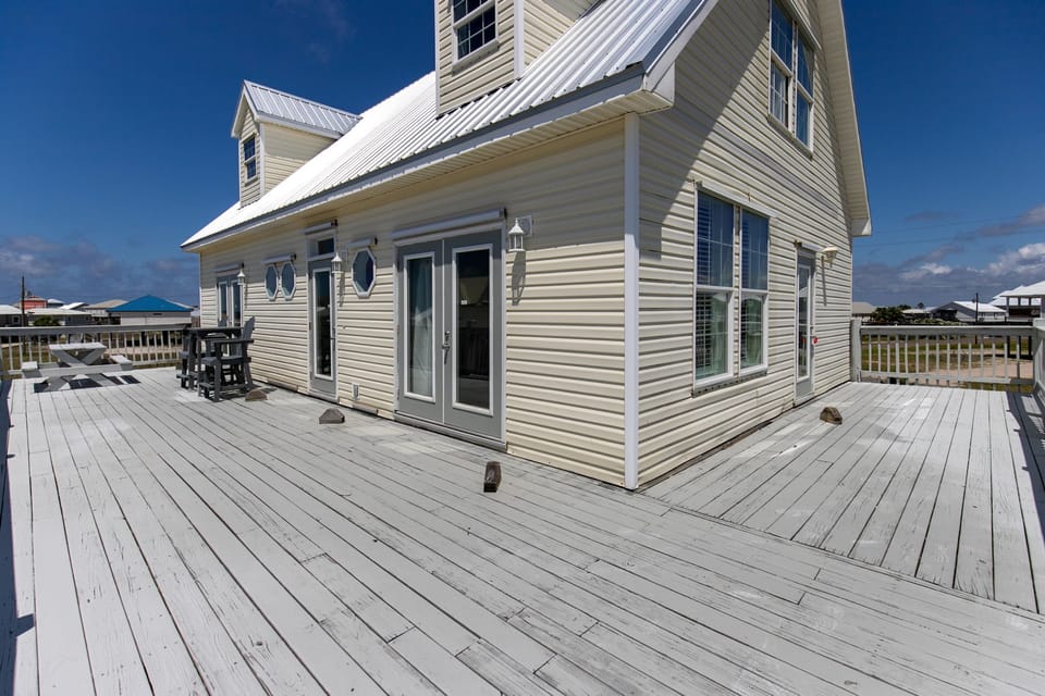 Spacious waterfront home with wraparound deck and coastal views, perfect for relaxing under bright blue skies.