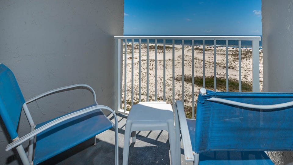 Enjoy a relaxing view from the balcony with blue chairs overlooking sandy dunes and the beach