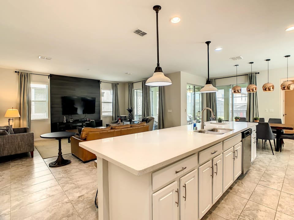 Spacious open kitchen with a large island, pendant lighting, and an inviting TV lounge opening to bright outdoor views.