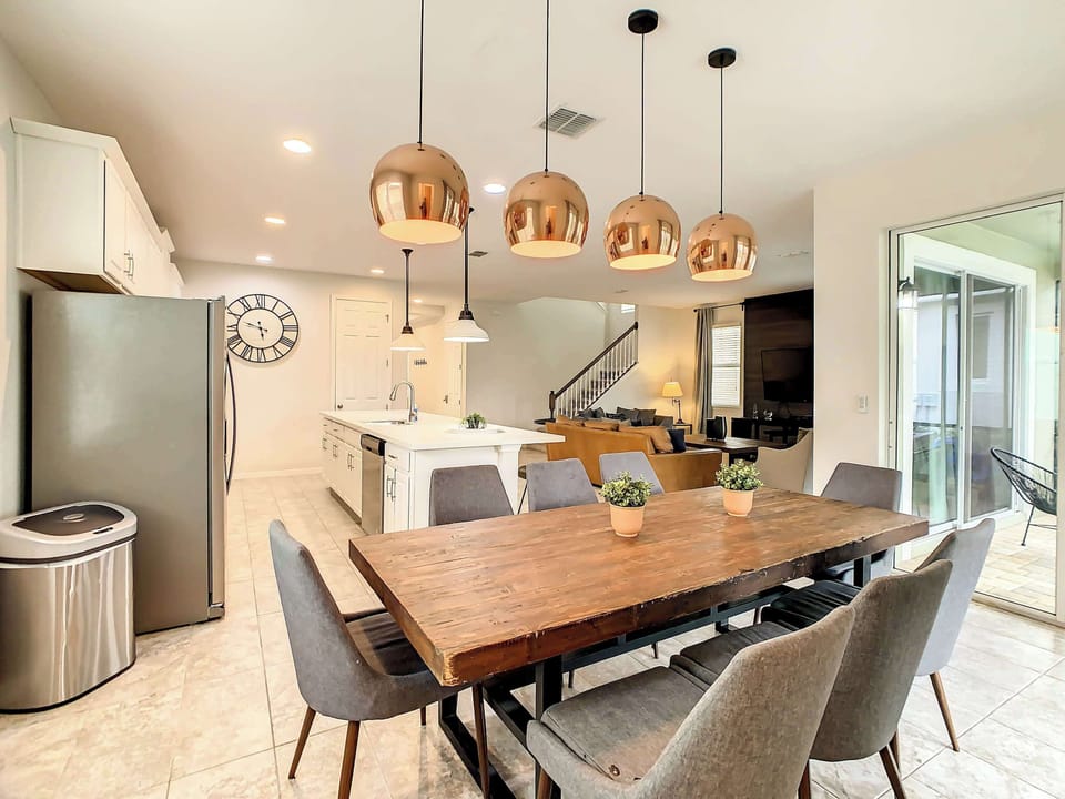 Open-plan dining area with seating for a large group, a bright white kitchen island, and striking copper pendant lights.