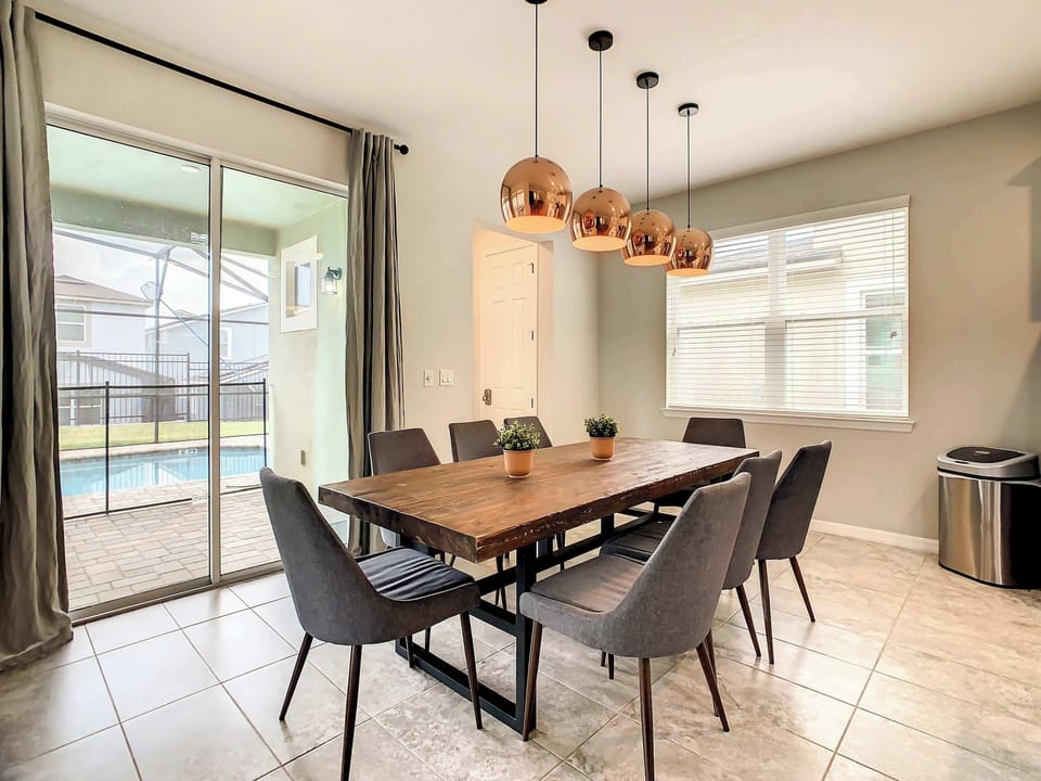 Private dining room with a rustic wood table, copper pendant lights, and sliding doors opening toward the pool patio.