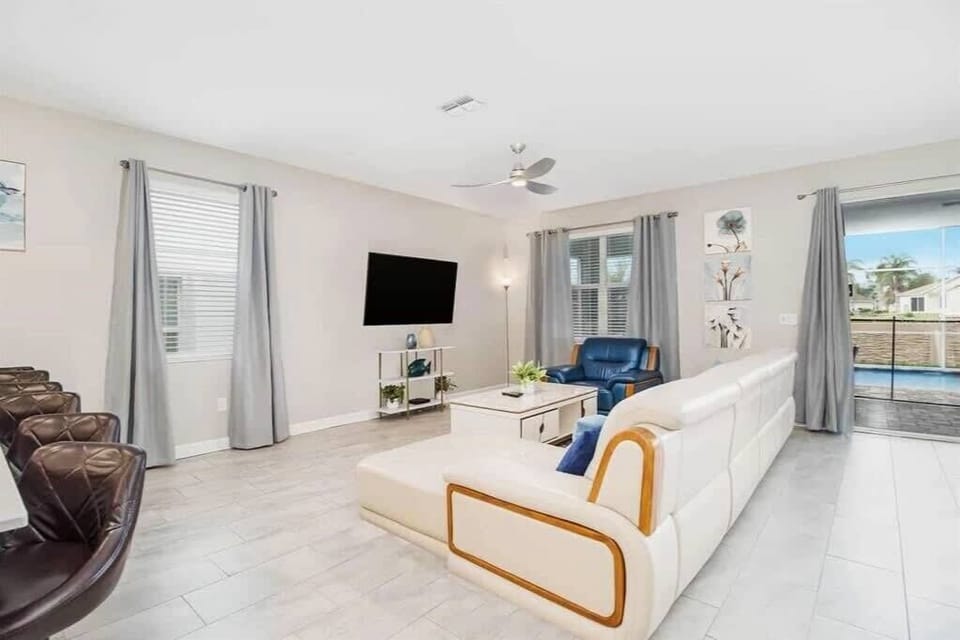 Spacious living room with a large white sectional, smart TV, and bright pool views through the glass doors.