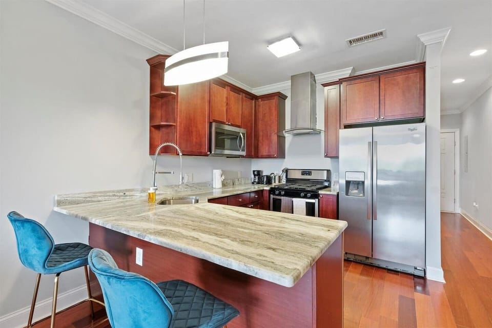 Fully equipped modern kitchen with spacious granite island, stainless steel appliances, and dining seating—perfect for meals or remote work.