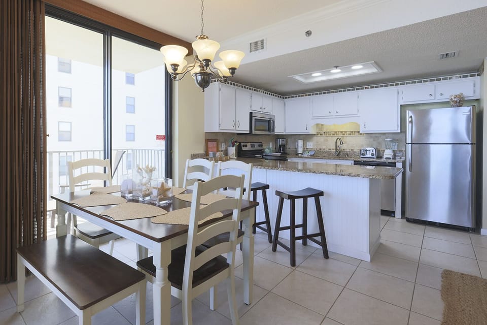 Bright dining area with a wooden table, white chairs, and a breakfast bar, seamlessly connecting to the kitchen and balcony