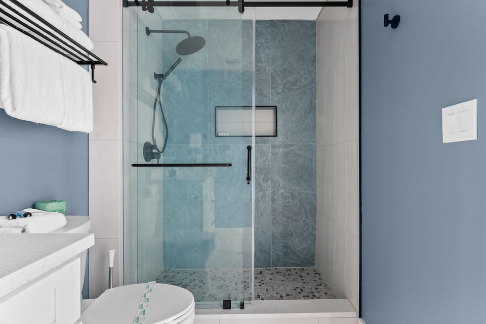 Step into your stylish bathroom featuring a spacious glass-enclosed shower with rainfall head and sleek mosaic tile floors for your daily refresh.