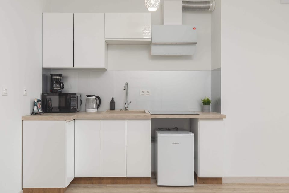A sleek kitchen with white cabinets and a light wooden countertop. Appliances and basic essentials are neatly arranged on the counter.